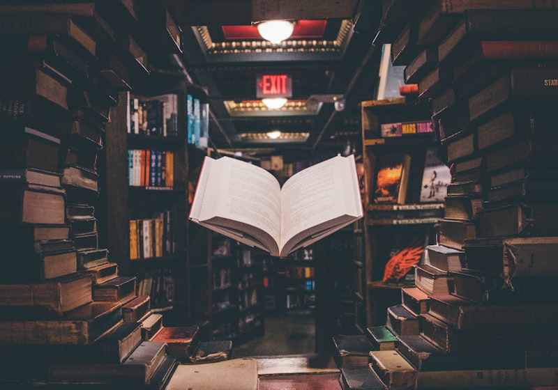 An open book in a library aisle lined with tall bookshelves.