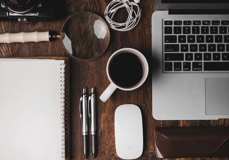 A neatly organised desk with a notebook, pens, coffee and a laptop.