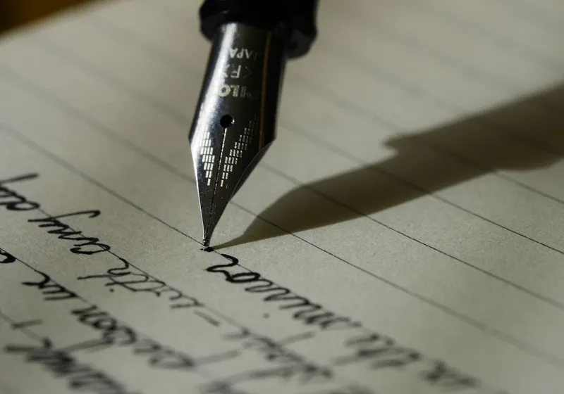 A fountain pen writing handwritten text on lined paper.