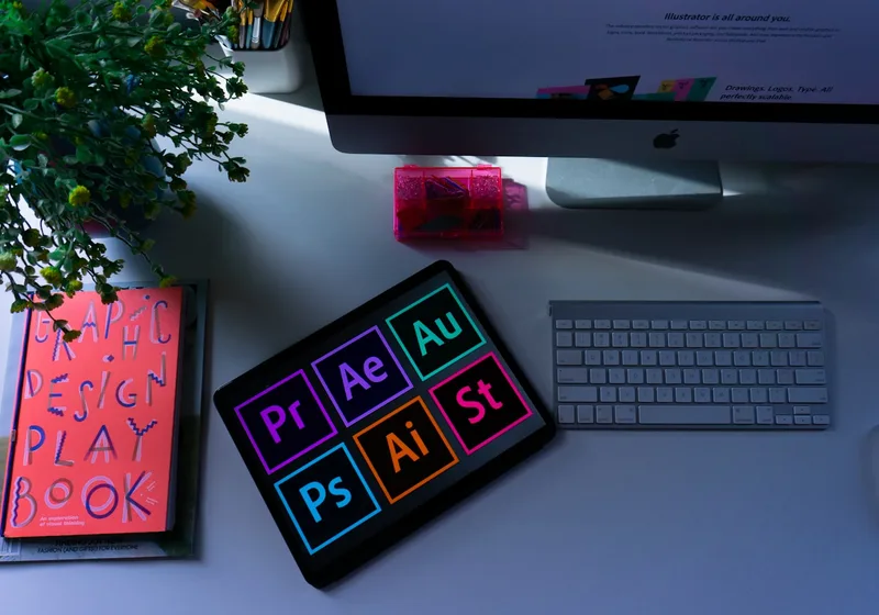 A design studio desk with creative-software icons and a colourful design playbook.