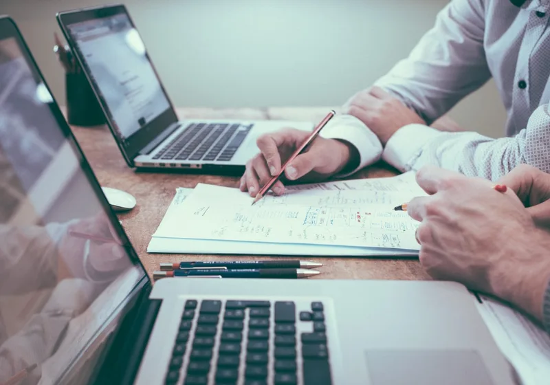 Two professionals reviewing a business report with a laptop and handwritten notes.